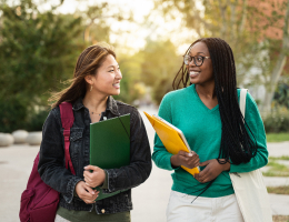 two young women holding notebooks outside